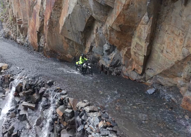 Adventure Motorcyclists Crossing Waterfall Cliff Road in Ladakh India
