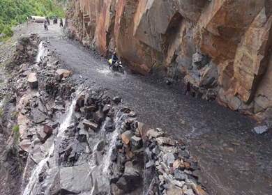 Adventure Motorcyclists Crossing Waterfall Cliff Road in Ladakh India