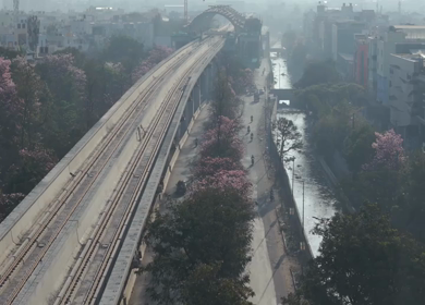 Aerial Slow Motion View of Metro Line and Road at Silk Board Junction with Pink Blossom Trees Bengaluru