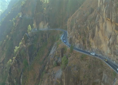 Aerial shot of car convoy passing through narrow cliff road in Kalpa Himachal Pradesh India