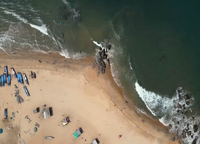 Aerial top view of fishing boats lined on sandy beach with waves in Kovalam Kerala India