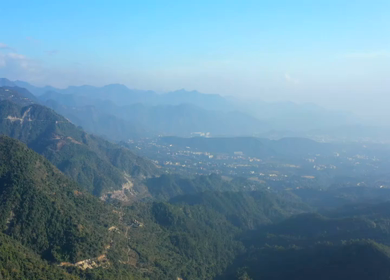 Aerial view of forest covered mountains under a blue sky with clouds in Uttarakhand, India