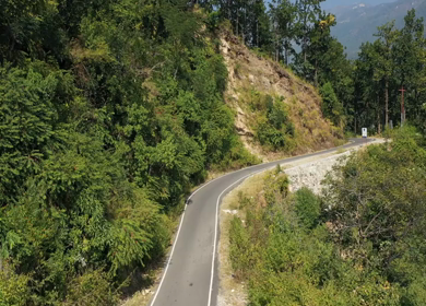 Aerial view of forest covered mountains under a blue sky with clouds in Uttarakhand, India