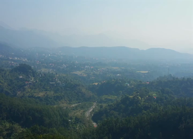 Aerial view of forest covered mountains under a blue sky with clouds in Uttarakhand, India