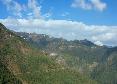 Aerial view of forest covered mountains under a blue sky with clouds in Uttarakhand, India