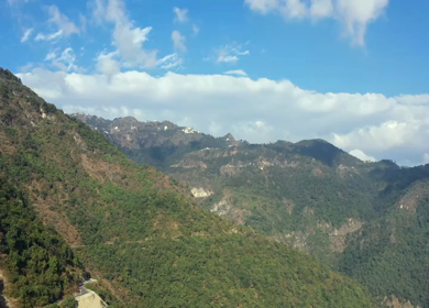 Aerial view of forest covered mountains under a blue sky with clouds in Uttarakhand, India