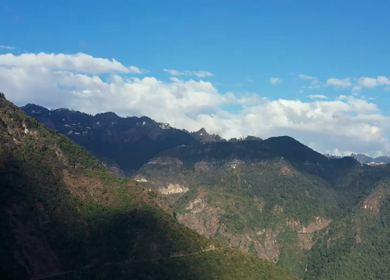 Aerial view of forest covered mountains under a blue sky with clouds in Uttarakhand, India