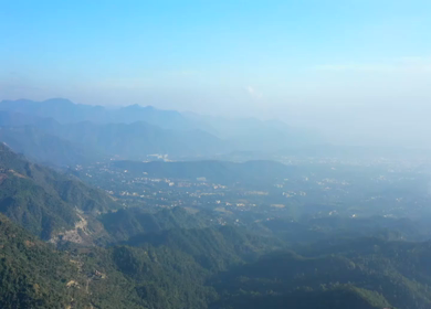 Aerial view of forest covered mountains under a blue sky with clouds in Uttarakhand, India
