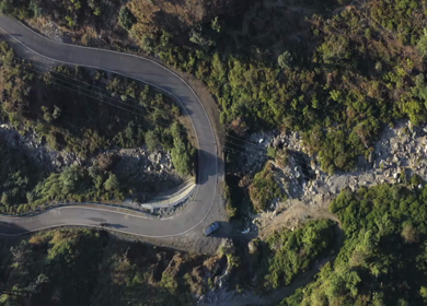 Aerial view of a sharp hairpin bend mountain road cutting through forested hills in Uttarakhand, India
