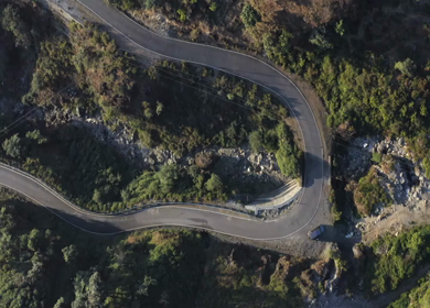 Aerial view of a sharp hairpin bend mountain road cutting through forested hills in Uttarakhand, India