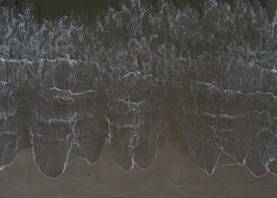 Aerial view of ocean waves washing onto a sandy beach in Phuket, Thailand