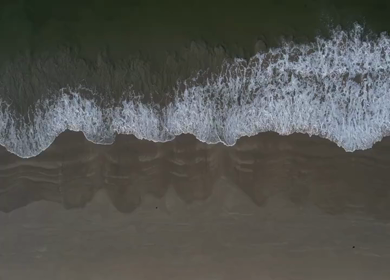 Aerial view of ocean waves washing onto a sandy beach in Phuket, Thailand