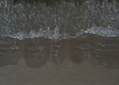 Aerial view of ocean waves washing onto a sandy beach in Phuket, Thailand