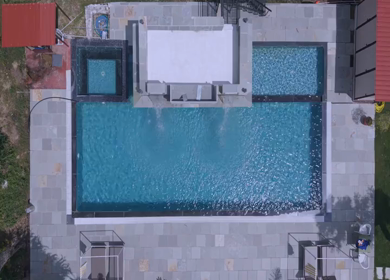 Top aerial view of luxury swimming pool surrounded by green forest landscape