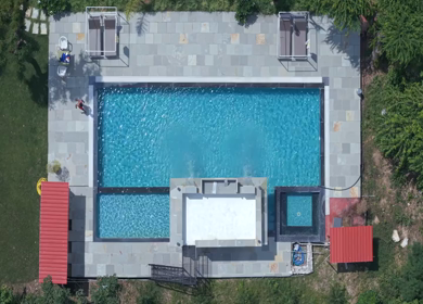 Top aerial view of luxury swimming pool surrounded by green forest landscape