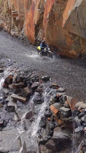 Vertical Aerial View of Adventure Motorcyclists Crossing Waterfall Stream in Ladakh