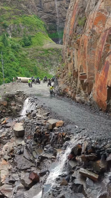 Vertical Aerial View of Adventure Motorcyclists Crossing Waterfall Stream in Ladakh