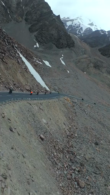 Vertical FPV Drone View of Adventure Motorcyclists Riding Through Snowy Mountain Pass in Ladakh