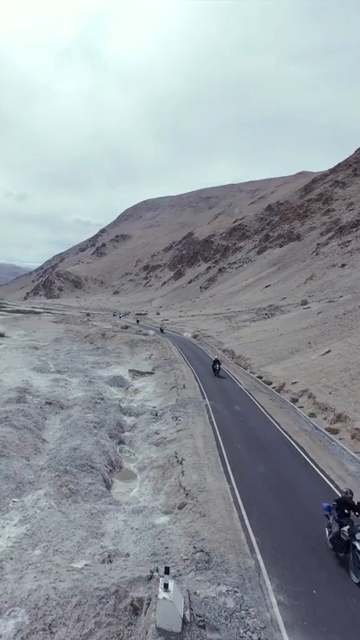 Vertical FPV Drone View of Adventure Motorcyclists Riding Through Snowy Mountain Pass in Ladakh