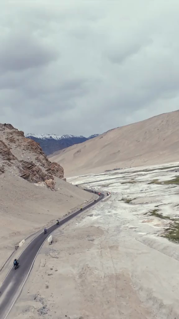 Vertical FPV Drone View of Adventure Motorcyclists Riding Through Snowy Mountain Pass in Ladakh