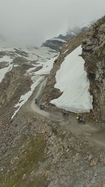 Vertical FPV Drone View of Adventure Motorcyclists Riding Through Snowy Mountain Pass in Ladakh