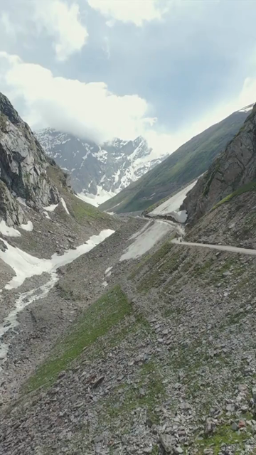 Vertical FPV Drone View of Adventure Motorcyclists Riding Through Snowy Mountain Pass in Ladakh