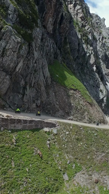 Vertical FPV Drone View of Adventure Motorcyclists Riding Through Snowy Mountain Pass in Ladakh