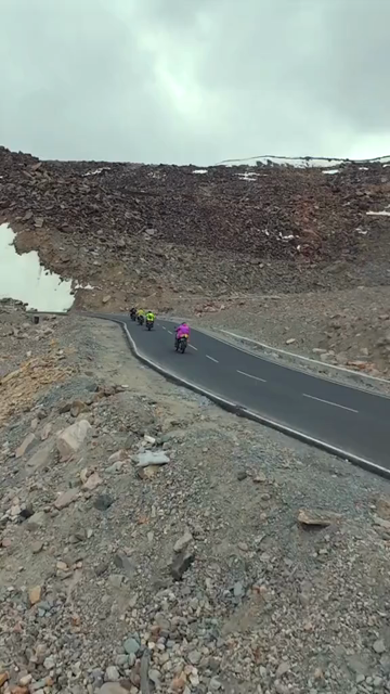 Vertical FPV Drone View of Adventure Motorcyclists Riding Through Snowy Mountain Pass in Ladakh