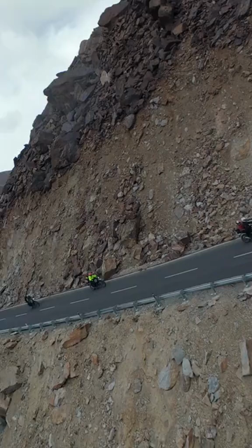 Vertical FPV Drone View of Adventure Motorcyclists Riding Through Snowy Mountain Pass in Ladakh