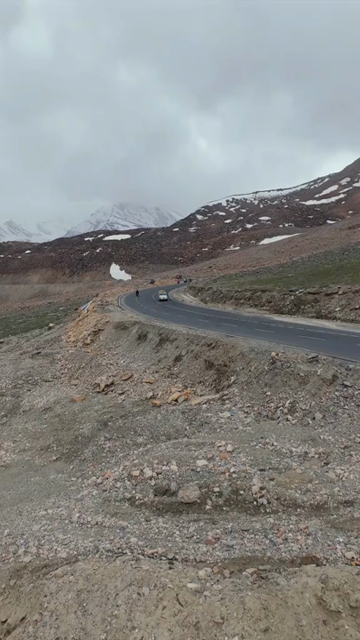 Vertical FPV Drone View of Adventure Motorcyclists Riding Through Snowy Mountain Pass in Ladakh