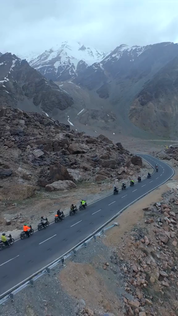 Vertical FPV Drone View of Adventure Motorcyclists Riding Through Snowy Mountain Pass in Ladakh