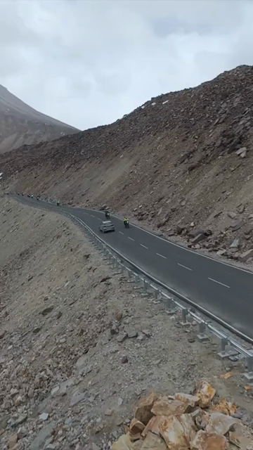Vertical FPV Drone View of Adventure Motorcyclists Riding Through Snowy Mountain Pass in Ladakh