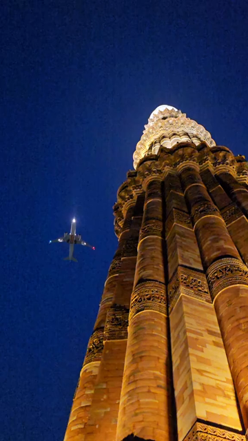 Vertical Night View of Qutub Minar with Airplane Flying Over Delhi India